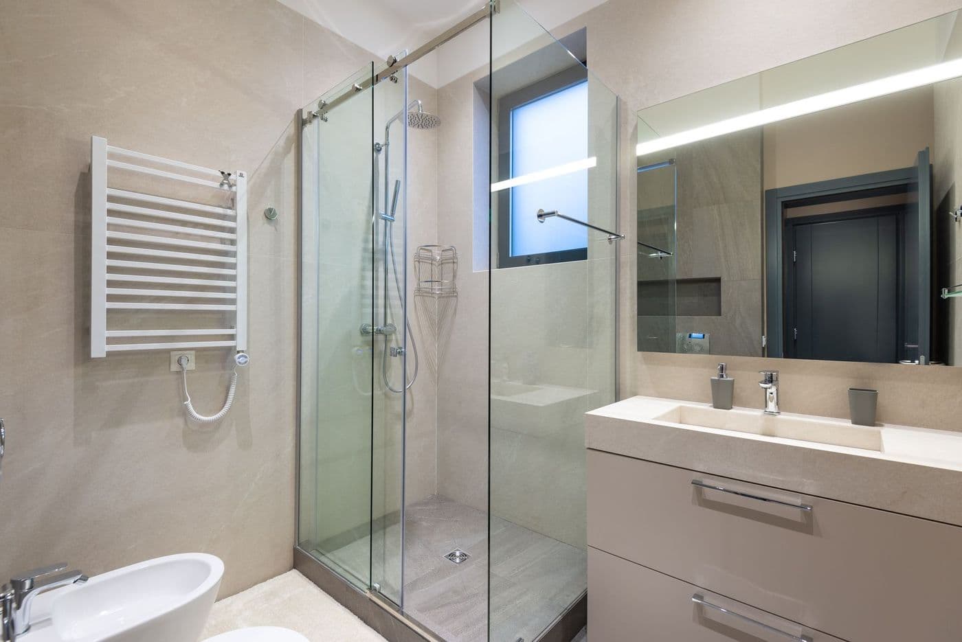 Shower cabin with glass walls near mirror hanging on wall above sink in modern minimalist styled bathroom